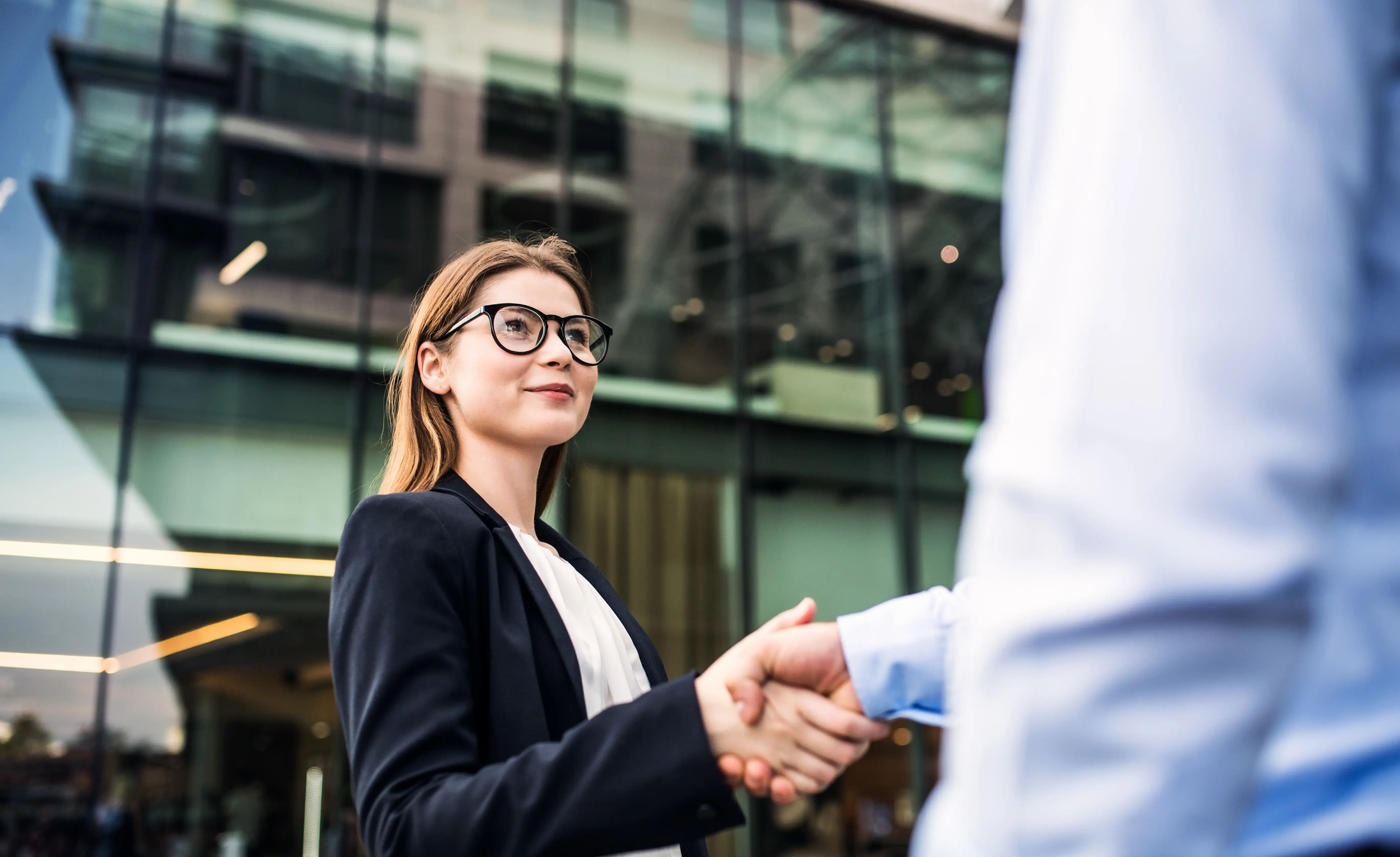 A young businesswoman and unrecognizable wealth manager shaking hands.